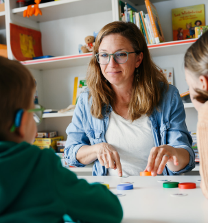 Kinder sitzen mit einer erwachsenen Person am Tisch und spielen eine Spiel