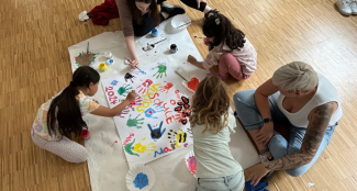 Eine Gruppe Kinder malt auf ein Tuch mit bunten Farben. 
